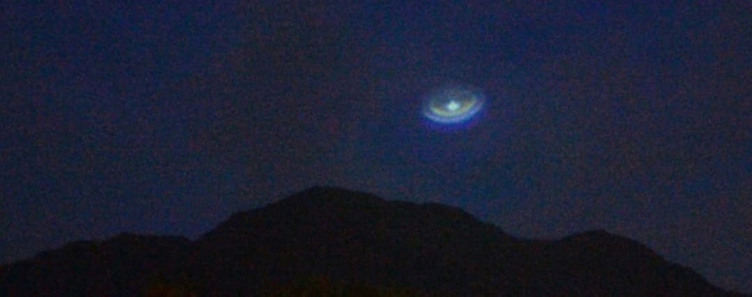 A light above the dark line of the hills at night